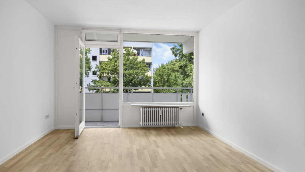 Empty living room with open balcony door and radiator in condominium in Munich Berg am Laim