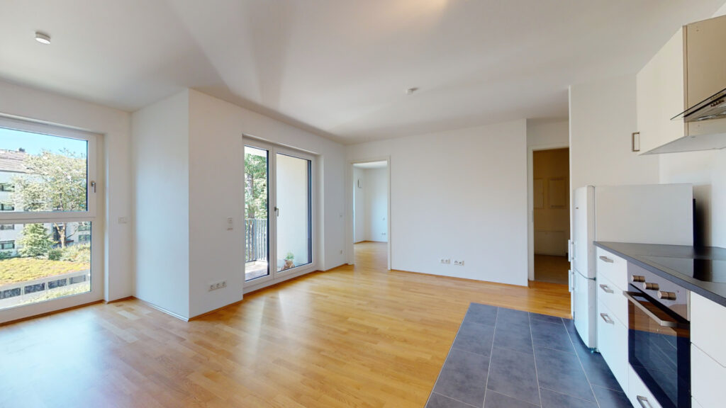 Living room with open kitchen and balcony access in an unfurnished new construction apartment in Munich-Berg am Laim