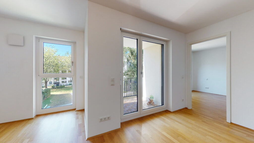 Empty living space with two balcony doors and a view of the hallway, newly built apartment in Munich-Berg am Laim