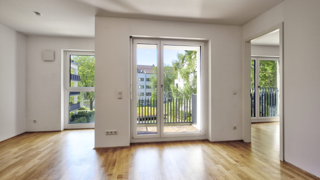 Sun-drenched empty room with two balcony doors in a new-build apartment in Munich-Berg am Laim
