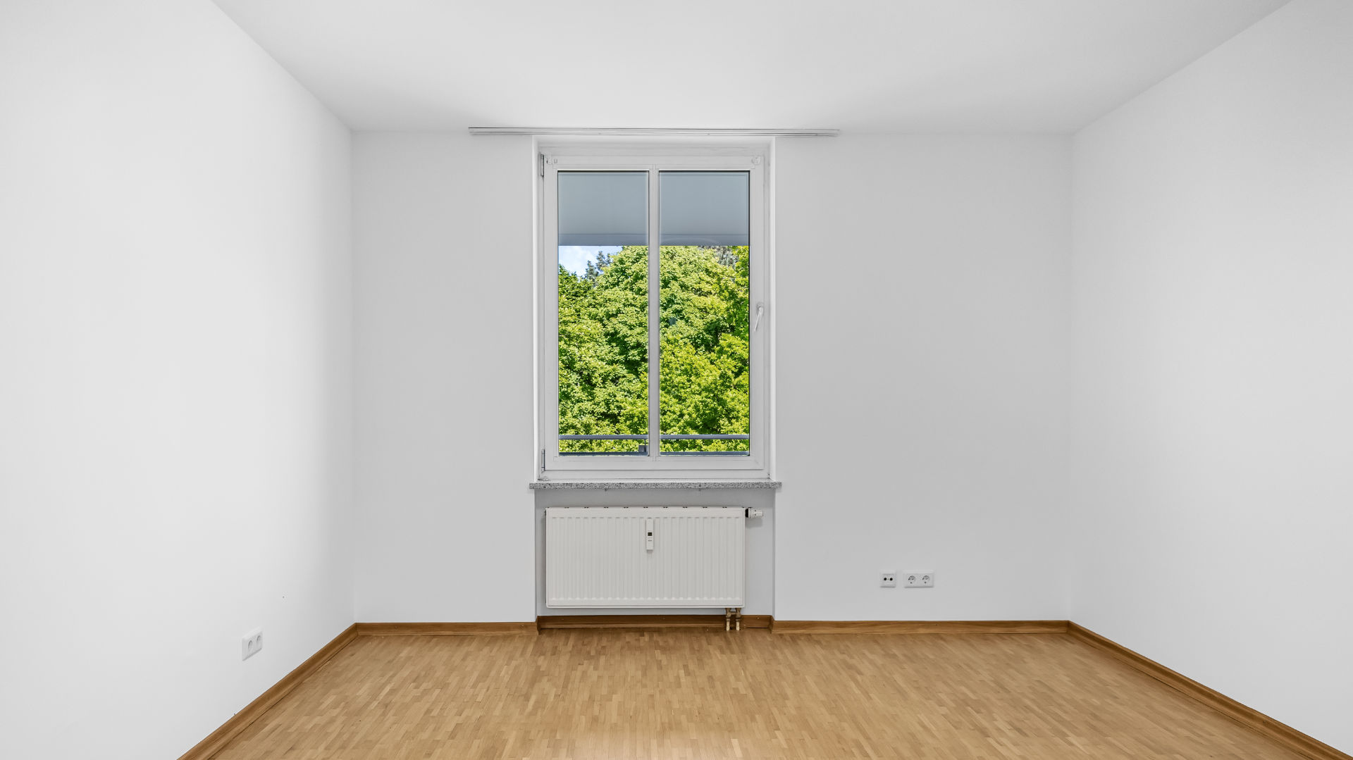 Unfurnished bedroom with parquet flooring and window with a green view in an apartment in Munich-Bogenhausen