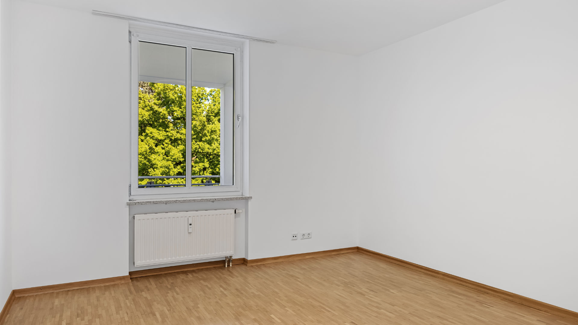 Unfurnished bedroom with parquet flooring and window with a green view in an apartment in Munich-Bogenhausen
