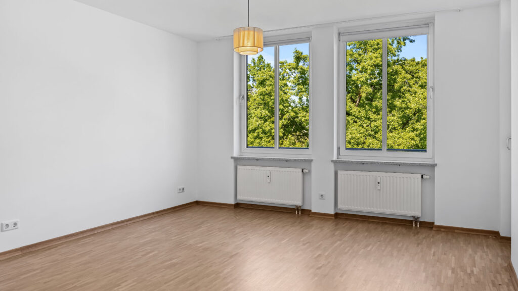 Unfurnished living room with parquet floor, ceiling light, and large window in an apartment in Munich-Bogenhausen