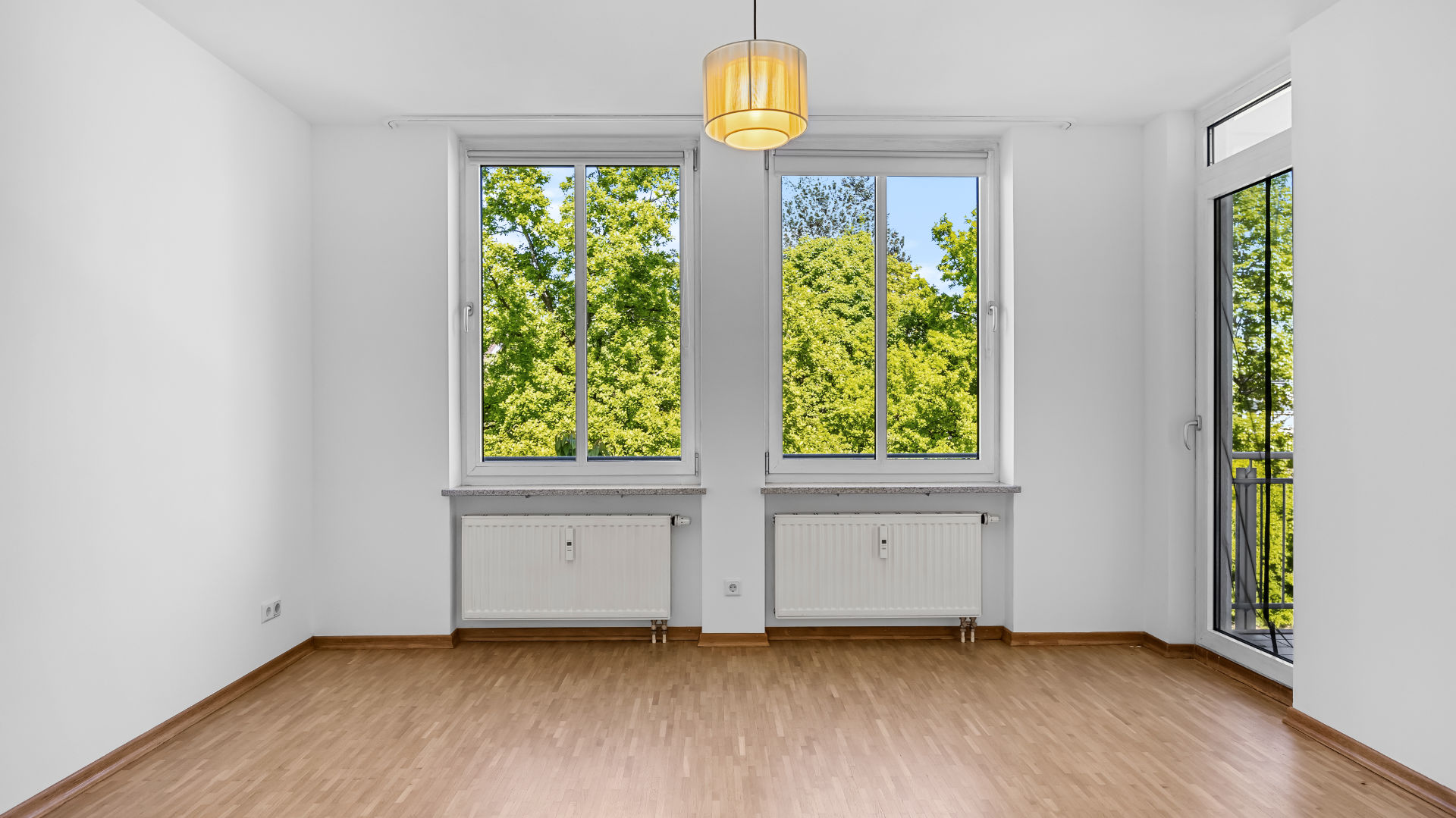 Unfurnished living room with parquet flooring, two windows, and balcony access in an apartment in Munich-Bogenhausen