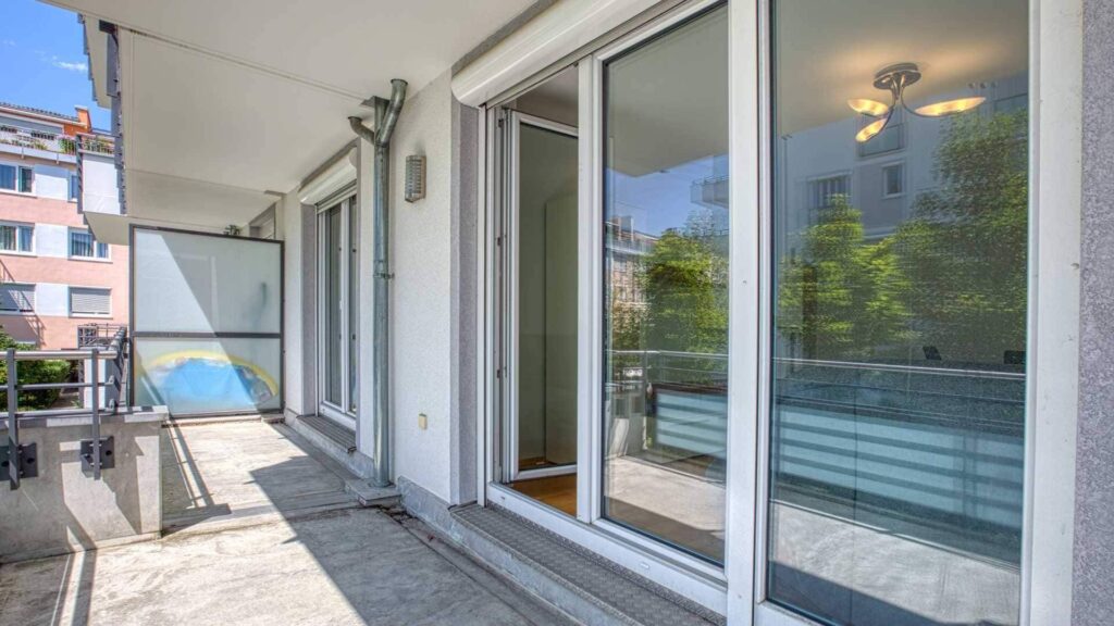 Balkon der Mietwohnung in Bogenhausen mit gefliestem Boden und Glasgeländer zur Terrasse