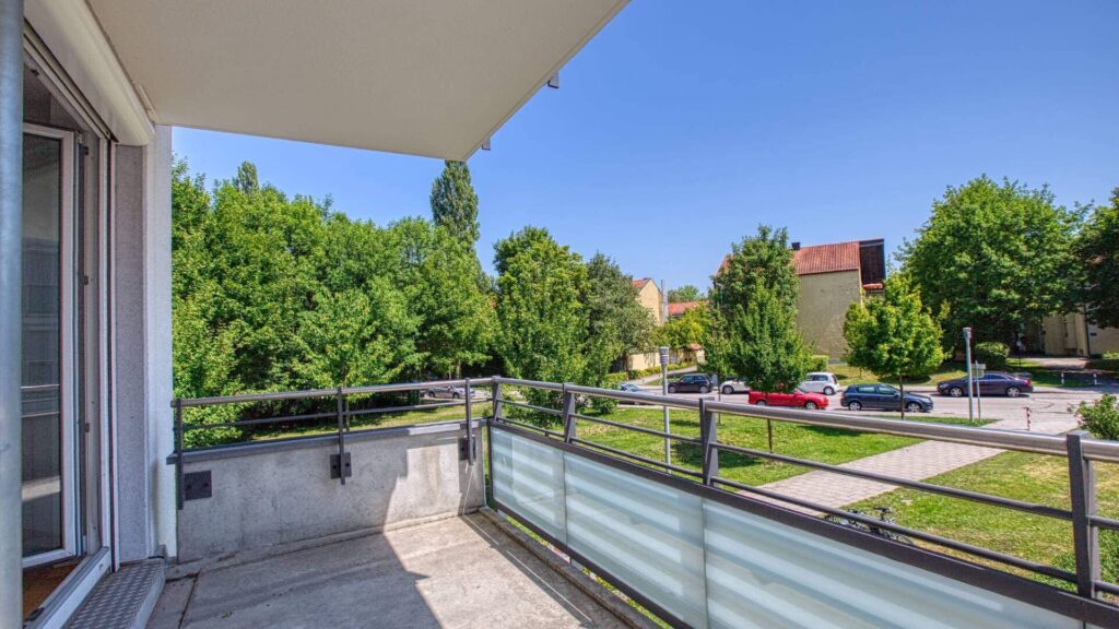 Balkon der Mietwohnung in Bogenhausen mit Glasgeländer und Blick auf grüne Bäume