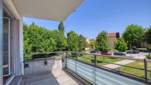 Balkon der Mietwohnung in Bogenhausen mit Glasgeländer und Blick auf grüne Bäume
