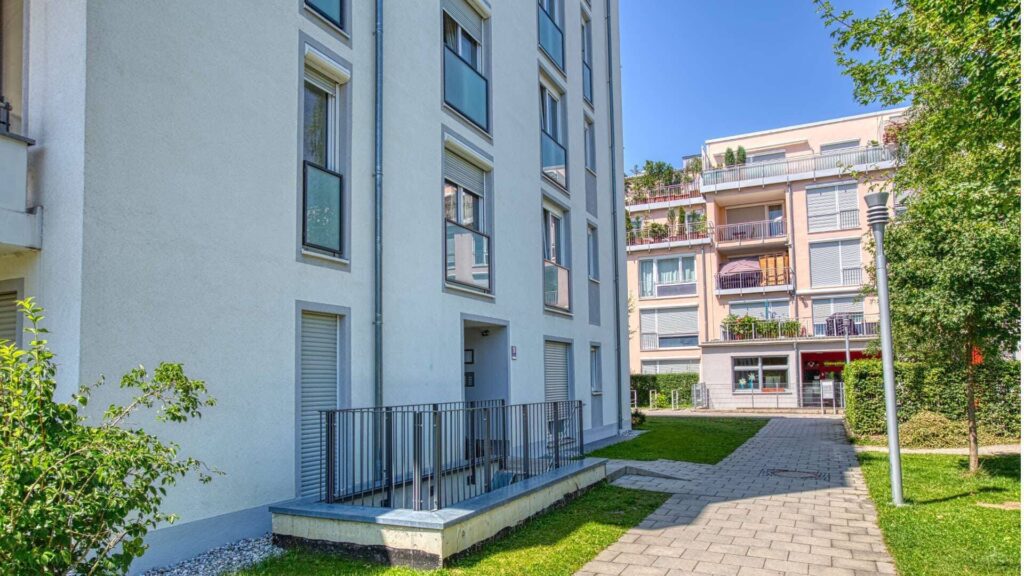 Gepflasterter Zugangsweg zu einem weißen Wohngebäude mit Grünanlage in Bogenhausen.