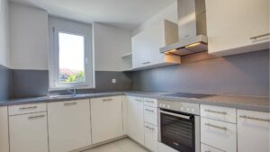 Weiße Einbauküche in Bogenhausen mit grauer Arbeitsplatte und Fenster.