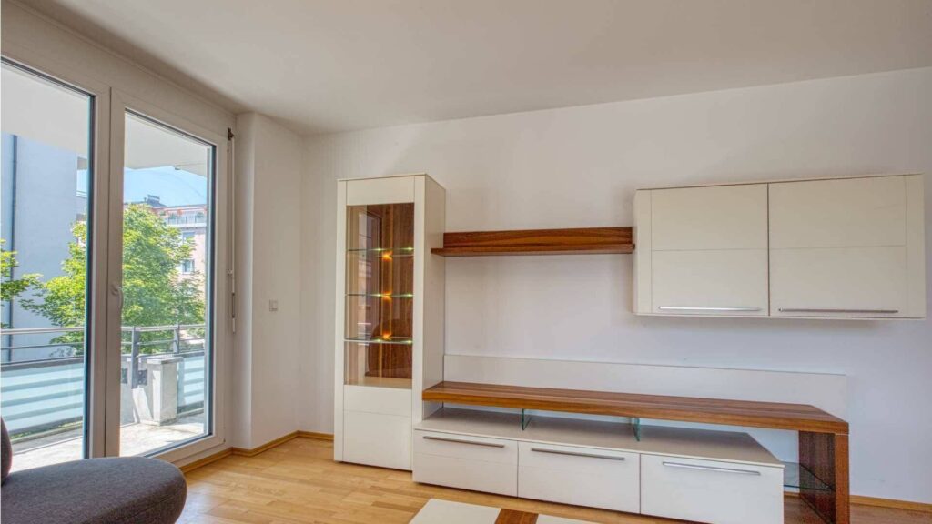 Wohnzimmer der Mietwohnung in Bogenhausen mit weißer Wohnwand, Vitrine und Balkonzugang