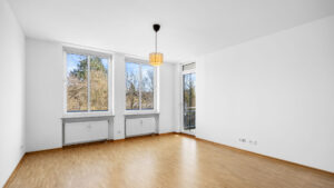 Empty living room with parquet floor, two windows, and patio door in Bogenhausen