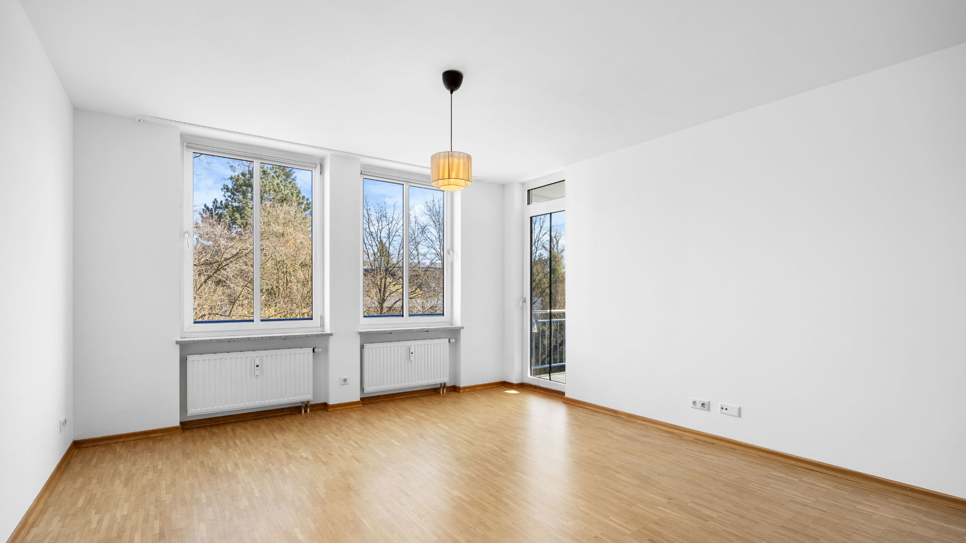 Empty living room with parquet floor, two windows, and patio door in Bogenhausen