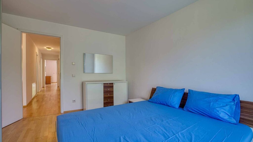 Schlafzimmer der Mietwohnung in Bogenhausen mit Doppelbett, blauer Bettwäsche und Holzboden