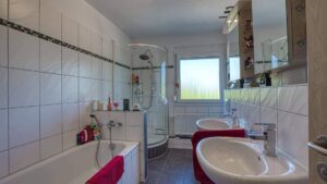 Badezimmer in Feldmoching mit Badewanne, Duschkabine, zwei roten Waschbecken und weiß gefliesten Wänden.