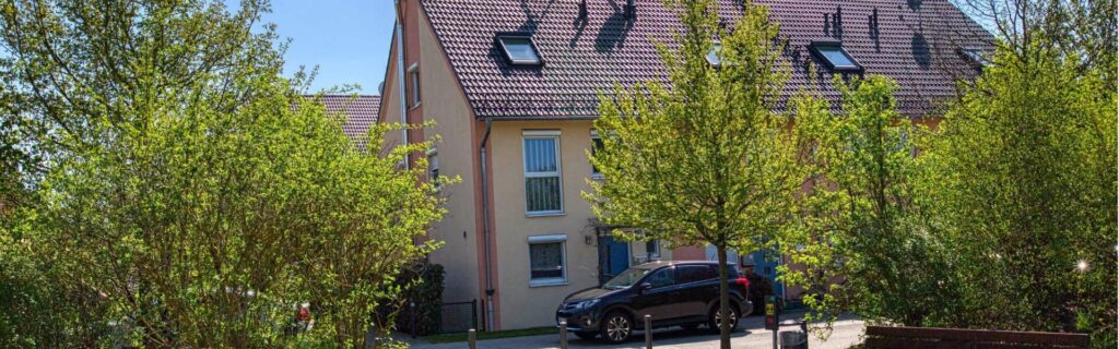 Außenansicht eines Hauses in Feldmoching mit Satteldach, Dachfenstern und Bäumen im Vordergarten.