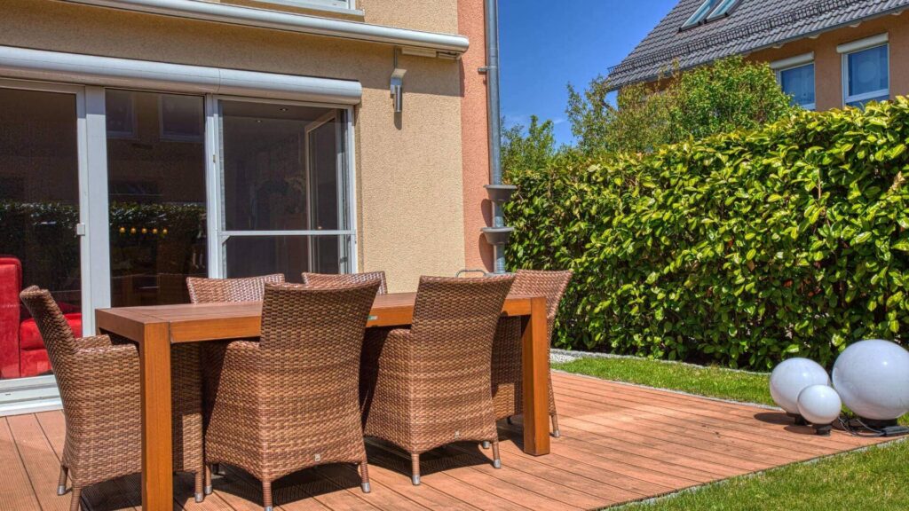 Terrasse mit Holzdielen, Sitzgruppe und Hecke im Garten des Hauses in München-Feldmoching