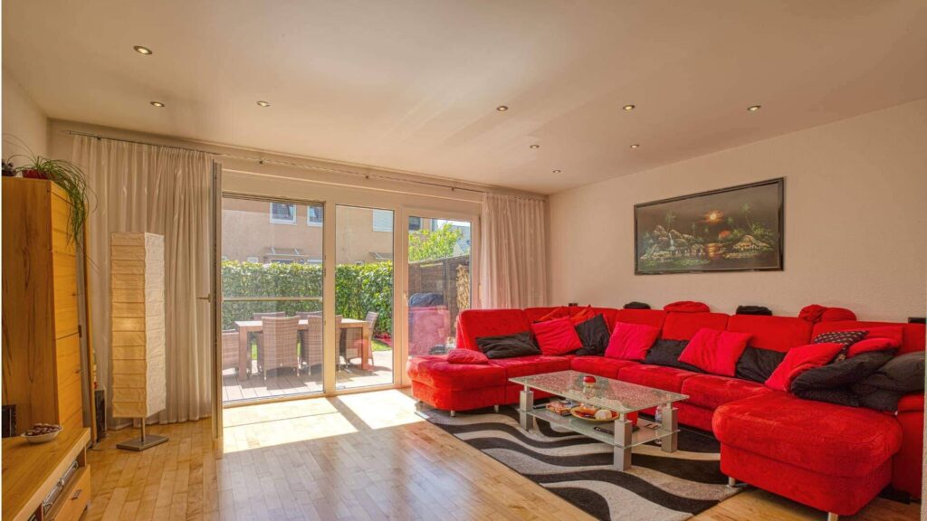 Helles Wohnzimmer in Feldmoching mit großem rotem Ecksofa, Terrassenzugang und Parkettboden.