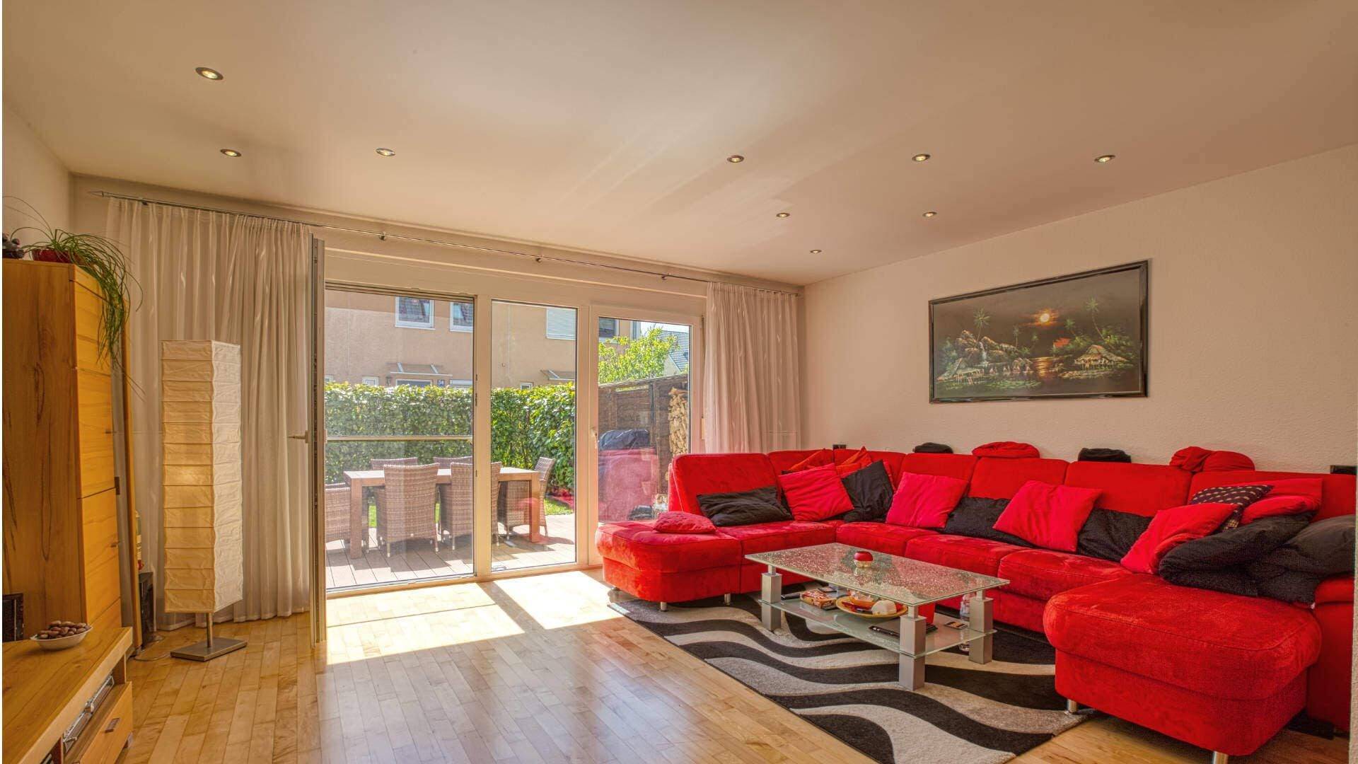 Bright living room in Feldmoching with a large red sectional sofa, terrace access, and parquet flooring.