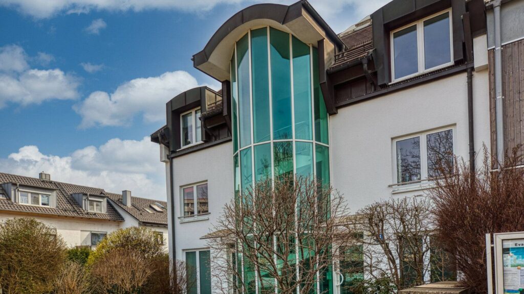 Facade of a residential building with a glass stair tower in Munich-Forstenried, Rogers Immobilien