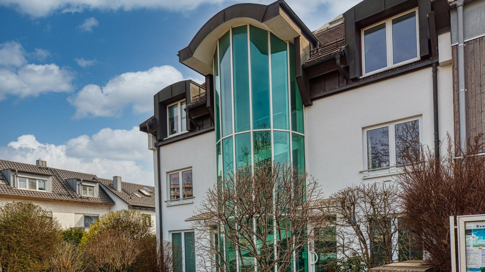Facade of a residential building with a glass stair tower in Munich-Forstenried, Rogers Immobilien