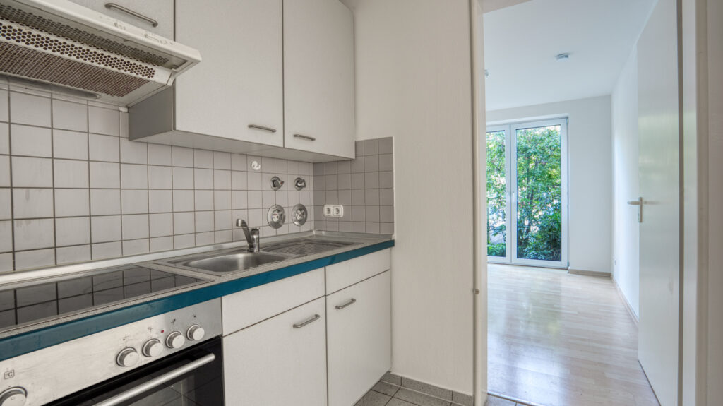Küche mit weißen Einbauschränken und Blick zur Terrassentür in einer Wohnung in München-Forstenried