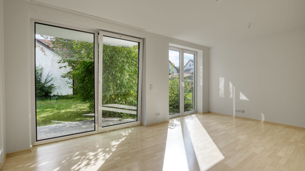 Wohnzimmer mit großer Fensterfront, Sonnenlicht und Gartenblick in München-Forstenried