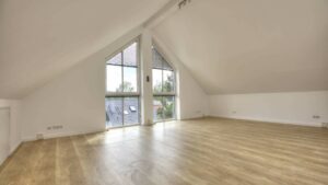 Leerer Dachgeschossraum mit spitz zulaufendem Fenster und hellem Holzboden in einem Büro in Fürstenried.