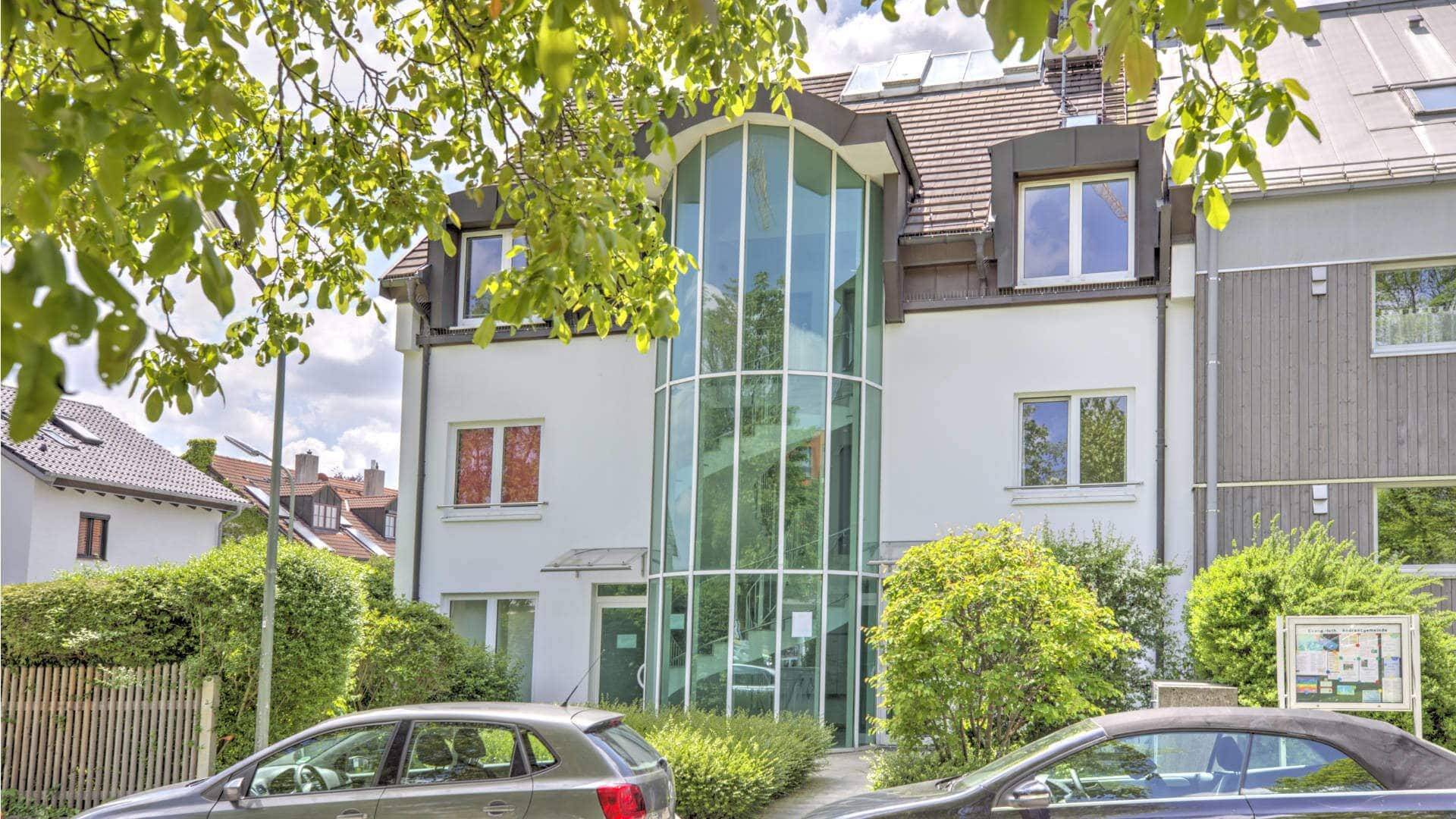 Außenansicht des Bürogebäudes in Fürstenried mit gläsernem Treppenturm, Bäumen und parkenden Autos