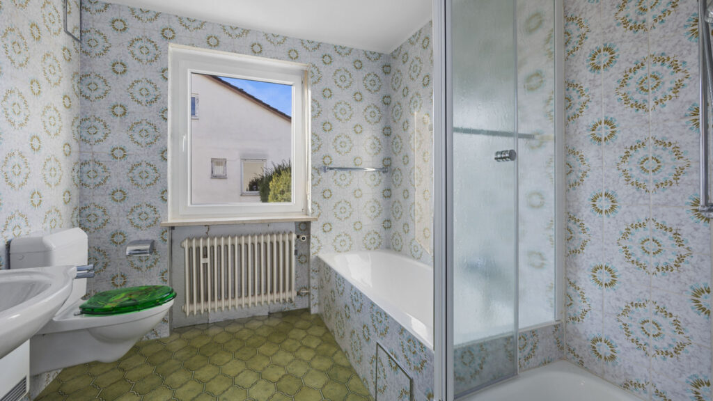 Unsaniertes Badezimmer mit floraler Tapete, grünem Fliesenboden und Duschkabine, Gauting