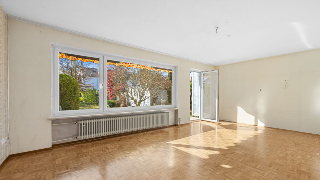 Weitläufiges, unmöbliertes Wohnzimmer mit Parkettboden und großer Fensterfront in einem Haus zum Kauf in Gauting