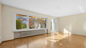 Weitläufiges, unmöbliertes Wohnzimmer mit Parkettboden und großer Fensterfront in einem Haus zum Kauf in Gauting