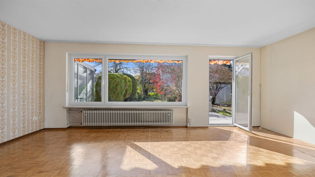 Lichtdurchflutetes, leeres Wohnzimmer mit Parkettboden und offener Terrassentür in einem Haus zum Kauf in Gauting