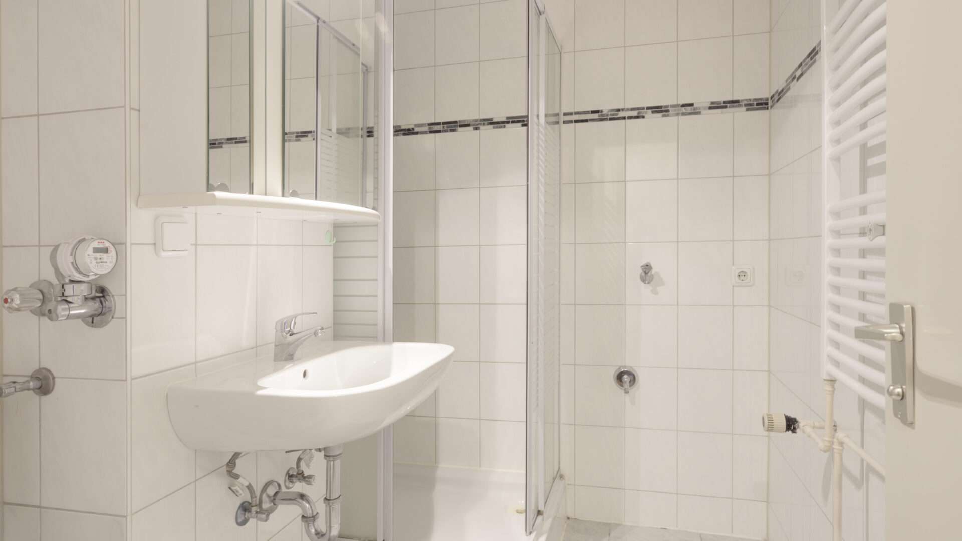 Älteres Badezimmer mit weißem Waschbecken, Fliesen und Handtuchheizkörper in einer Wohnung in München-Giesing