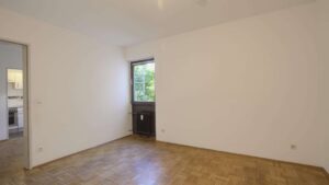 Unmöbliertes Zimmer mit Parkettboden, Kachelofen und Fenster in einer Wohnung in München-Giesing