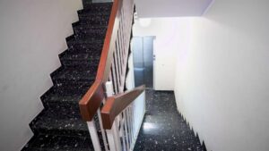 Treppenhaus mit dunklem Steinboden, Holzhandlauf und Wohnungstür in einem Mehrfamilienhaus in München-Giesing