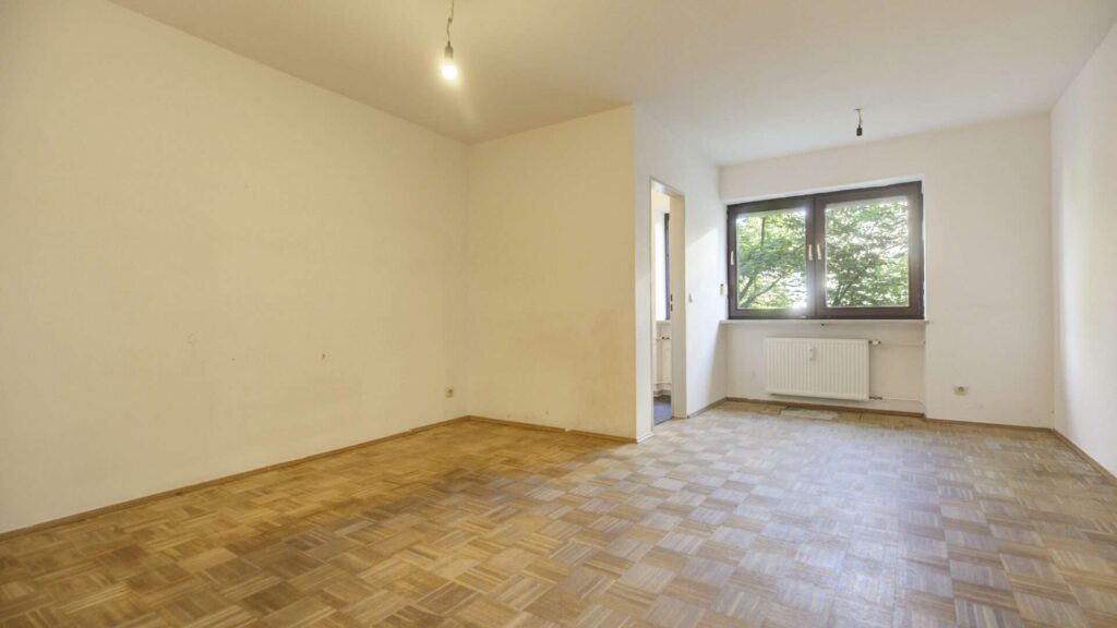 Unfurnished living room with parquet floor, large window and heating radiator in an apartment in Munich-Giesing