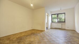 Unmöbliertes Wohnzimmer mit Parkettboden, großem Fenster und Heizkörper in einer Wohnung in München-Giesing