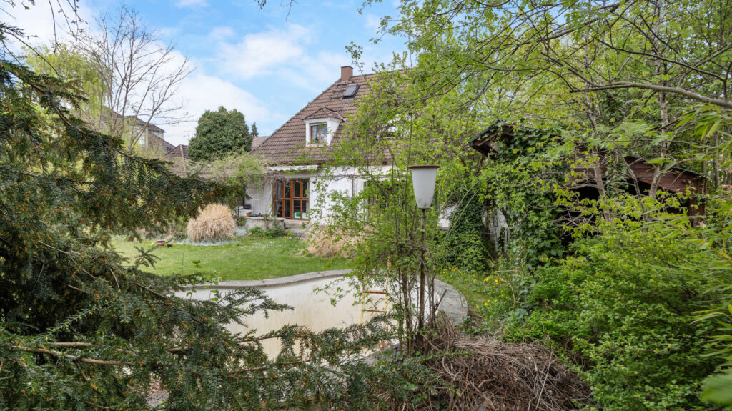Rear garden of the property in Großhadern with an ivy-covered house, outbuilding, and old pool