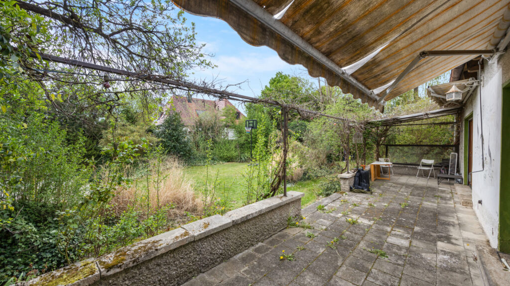 Paved terrace with awning and seating area on the property in Großhadern, view towards the garden