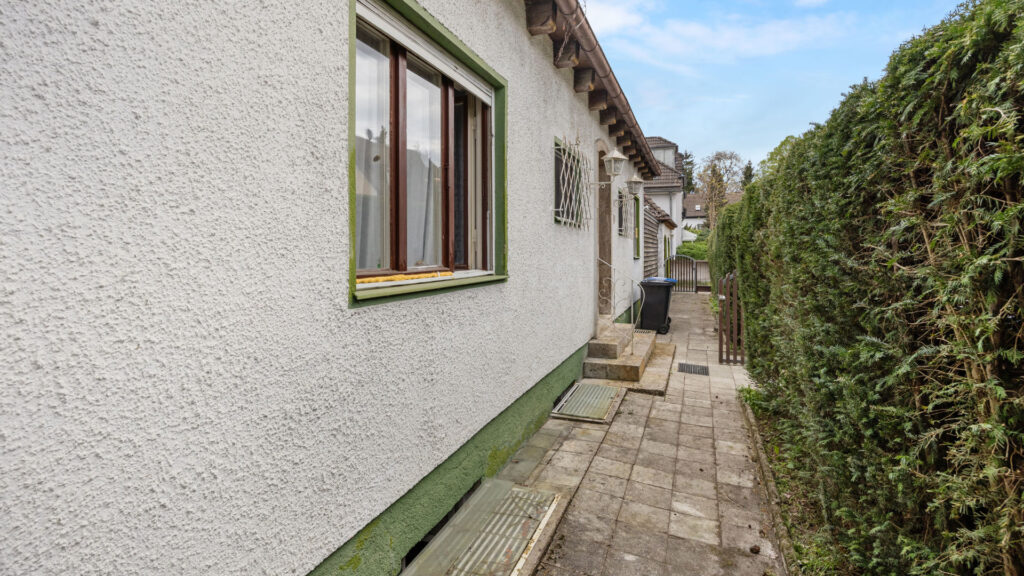 Paved path along the house facade on the property in Großhadern with green window frames