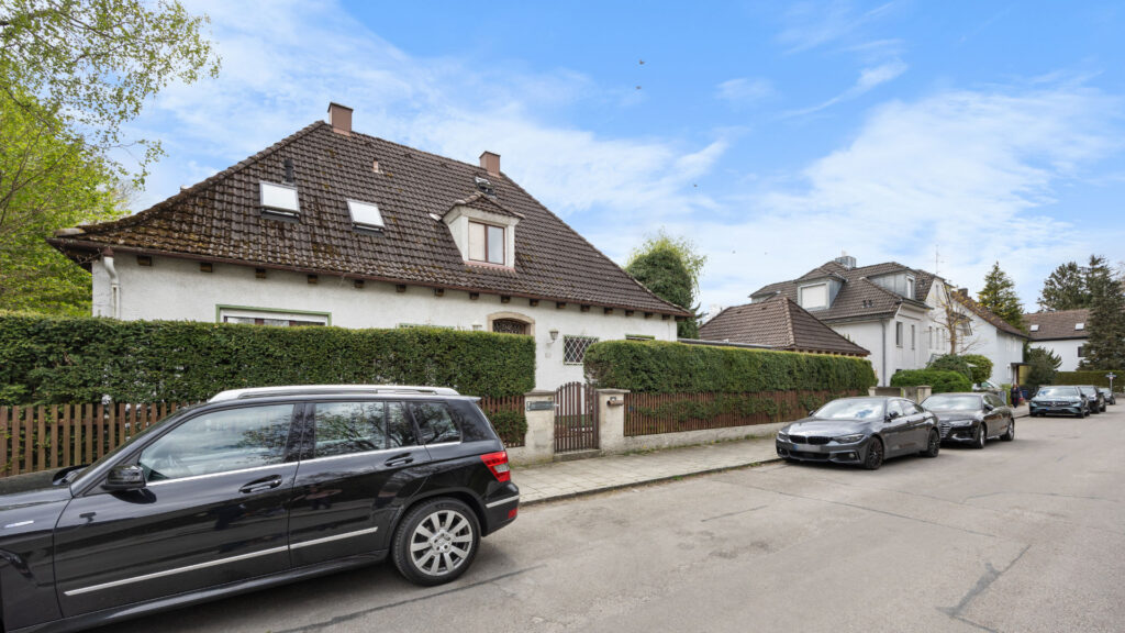 Street in front of the property in Großhadern with an existing house behind a hedge and parked cars