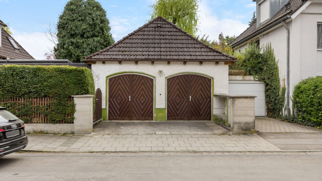 Detached double garage with a tiled roof and carved wooden doors on the property in Großhadern