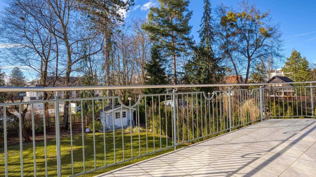Balkon mit Metallgeländer und Blick auf Bäume und Nachbarhäuser in München-Hadern.