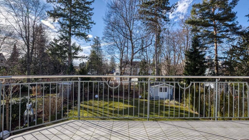 Balkon mit Metallgeländer und Blick auf Bäume und Gartenhäuschen der Wohnung in München-Hadern