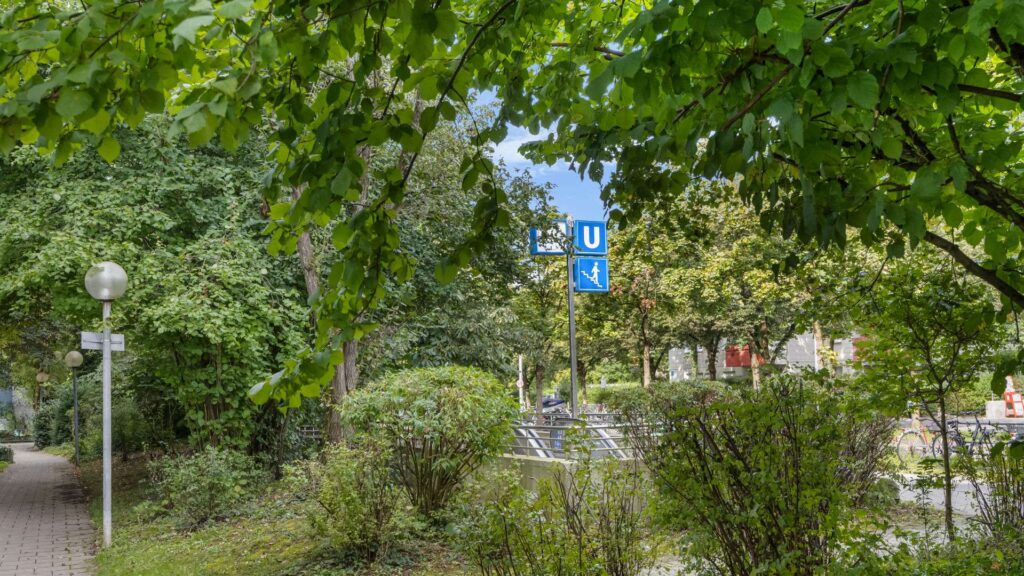 Greened walkway with trees and subway sign in the area of the apartment in Hadern