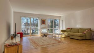 Wohnzimmer mit grünem Sofa, Teppich und großen Fenstern in einer Wohnung in München-Hadern