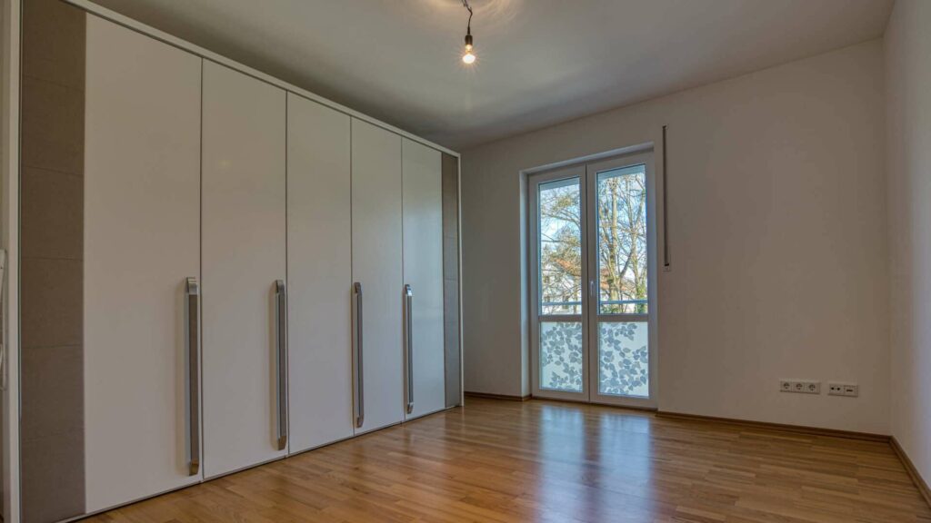 Leeres Zimmer mit raumhohen Einbauschränken und Balkonzugang in der Wohnung in München-Hadern