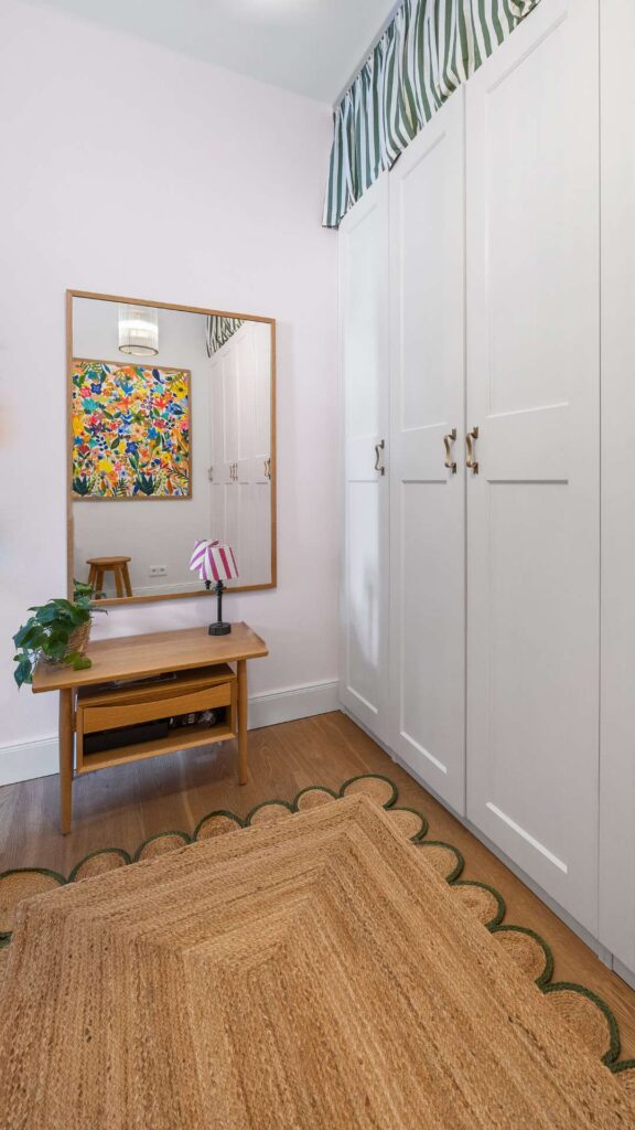 Ankleidezimmer der Altbauwohnung Haidhausen mit weißen Schränken, Wandspiegel und buntem Kunstdruck