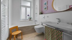 Bathroom of the old building apartment in Haidhausen with bathtub, window, wooden chair, and wall-mounted toilet