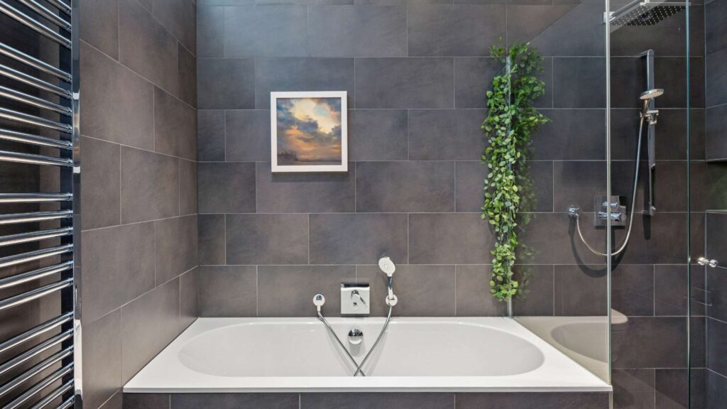 Bad der Altbauwohnung Haidhausen mit Badewanne, Regendusche, dunklen Fliesen und hängender Grünpflanze